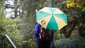 Person walking on campus with a University of Oregon umbrella