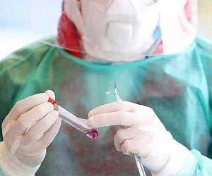Person wearing PPE while holding a test tube