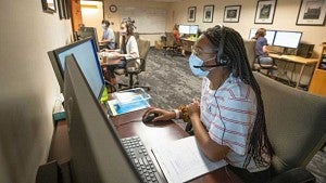 Student members of the Corona Corps working at computers while wearing masks