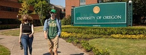 Two students wearing masks walking near the University of Oregon entrance sign