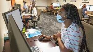 Corona Corps members working at computers while being physically distant and wearing masks.