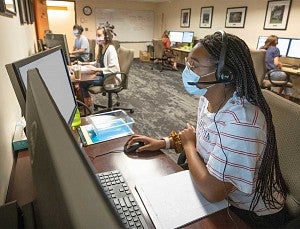 Corona Corps members working at computers while physically distanced and wearing masks