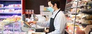Housing and Dining Man wearing a mask while using a cash register at a grocery store