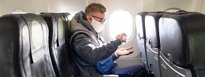 Travel Man wearing a mask while applying hand sanitizer while sitting in a window seat on an airplane